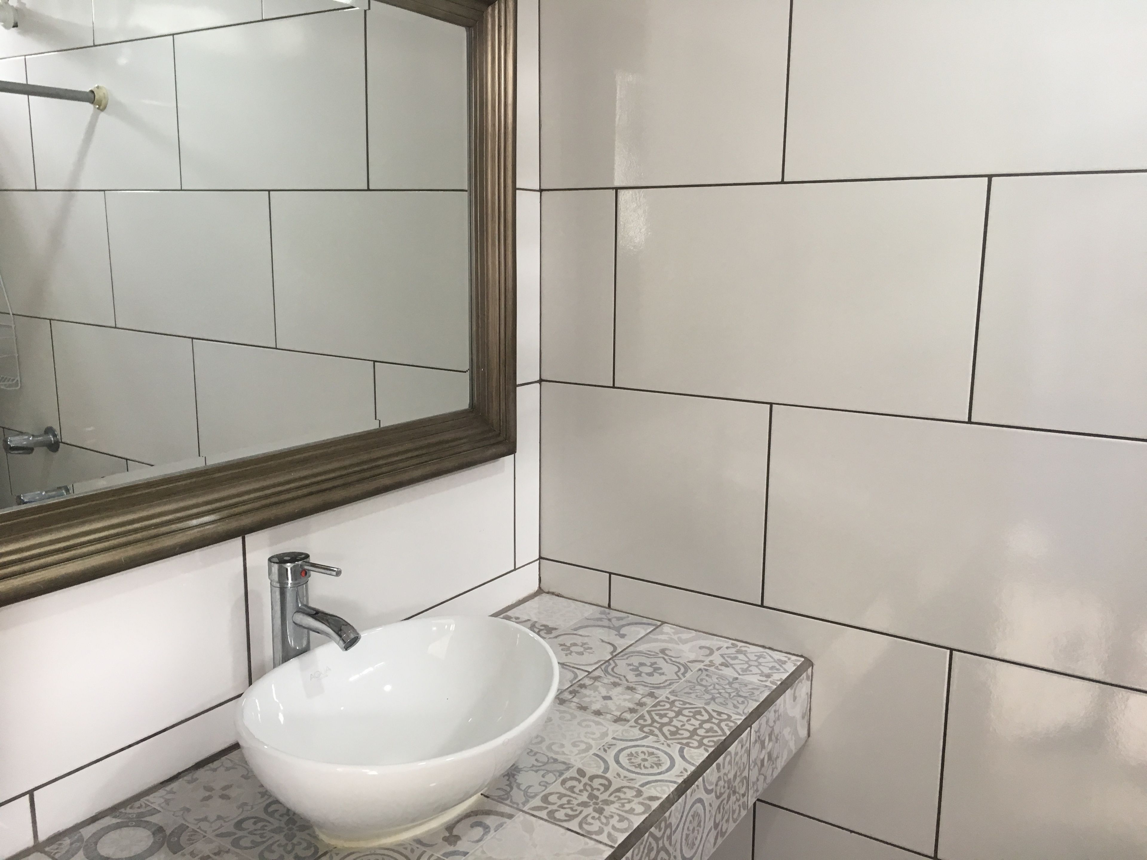 Un bagno con un lavandino bianco, uno specchio e piastrelle decorate.