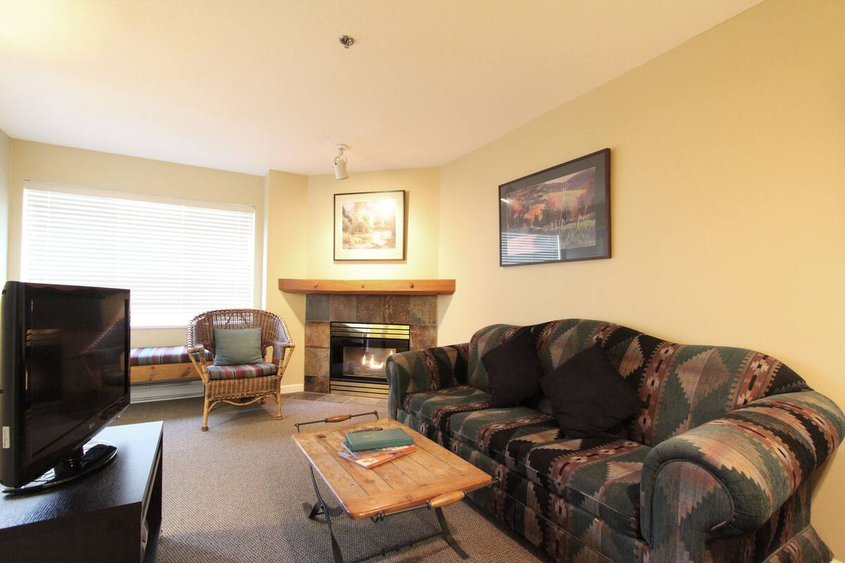 Una sala de estar con chimenea, televisión, sofá y sillón.