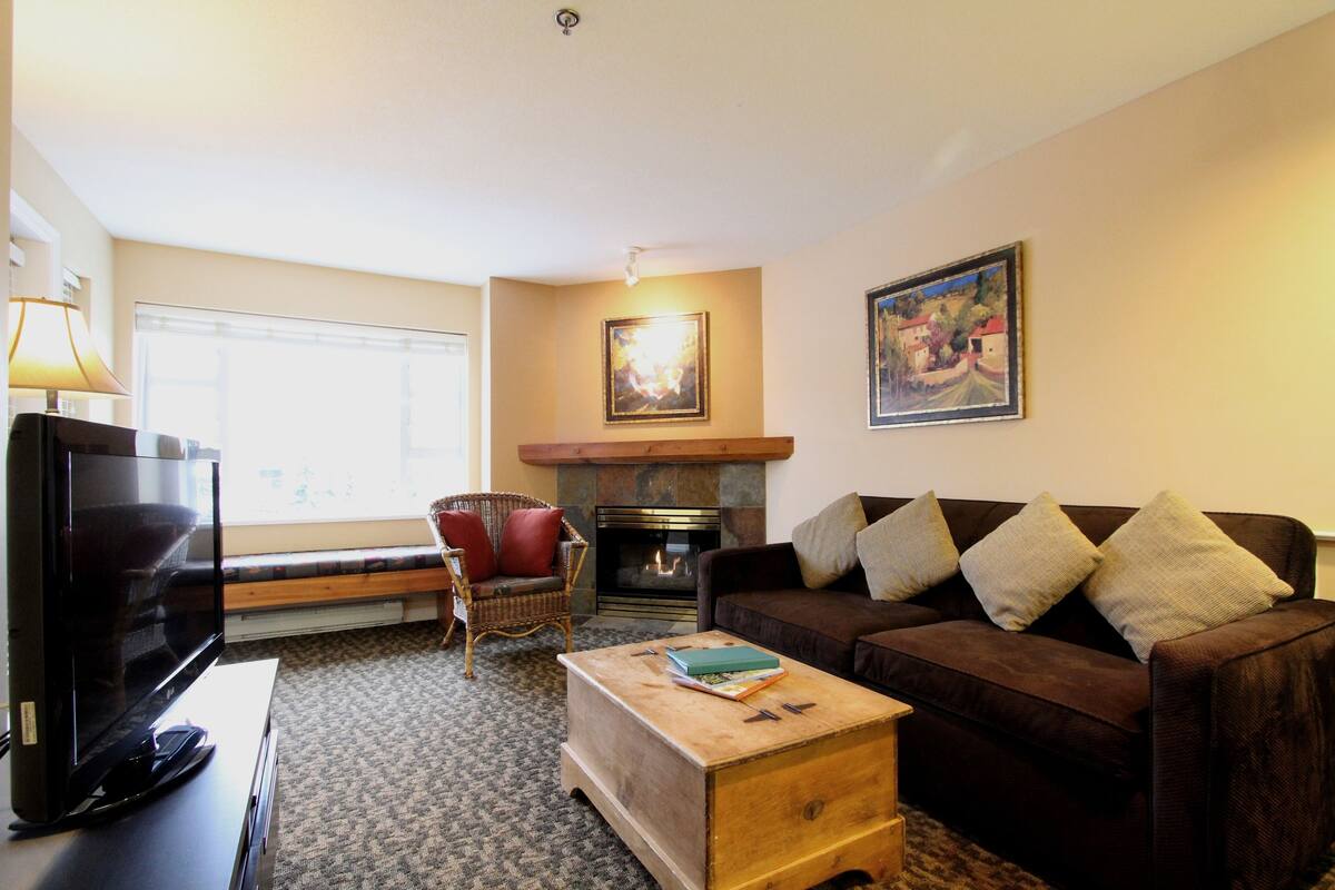 Una sala de estar con televisión, sofá, mesa de centro de madera y chimenea.