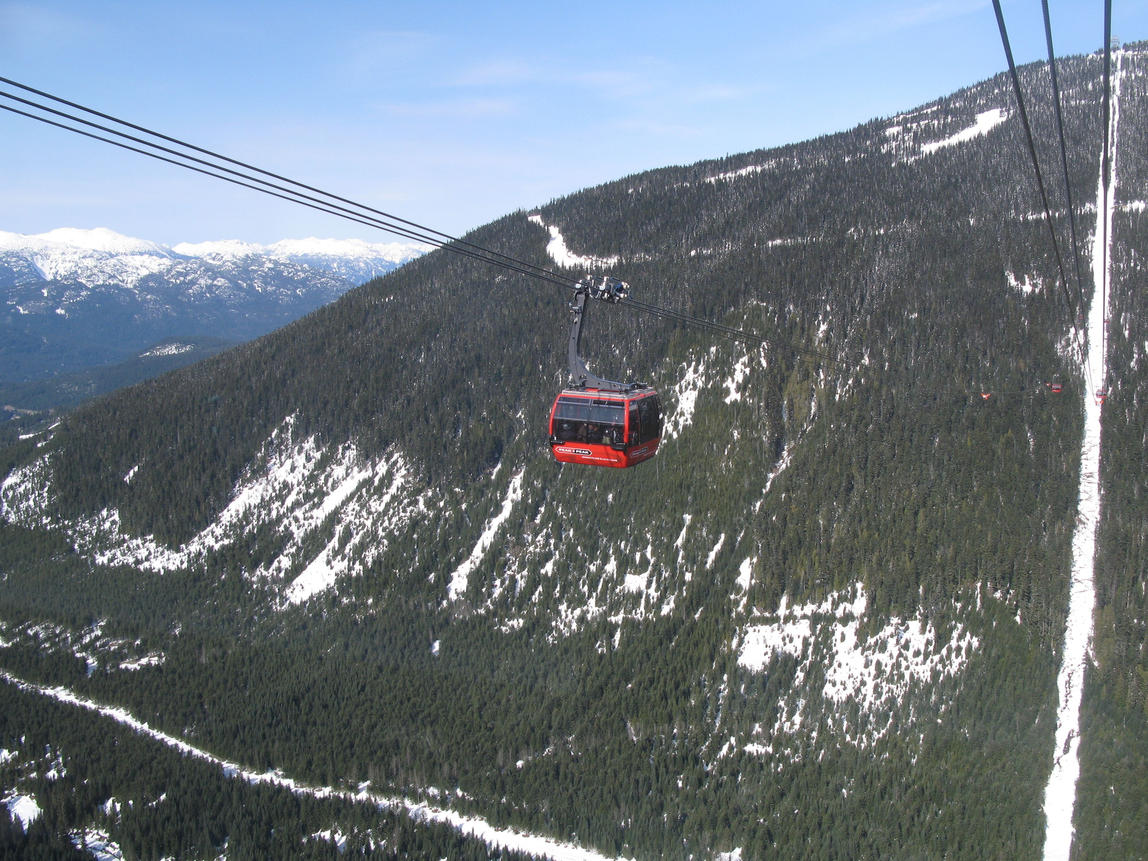 Eine rote Seilbahn fährt einen verschneiten Berg hinauf.