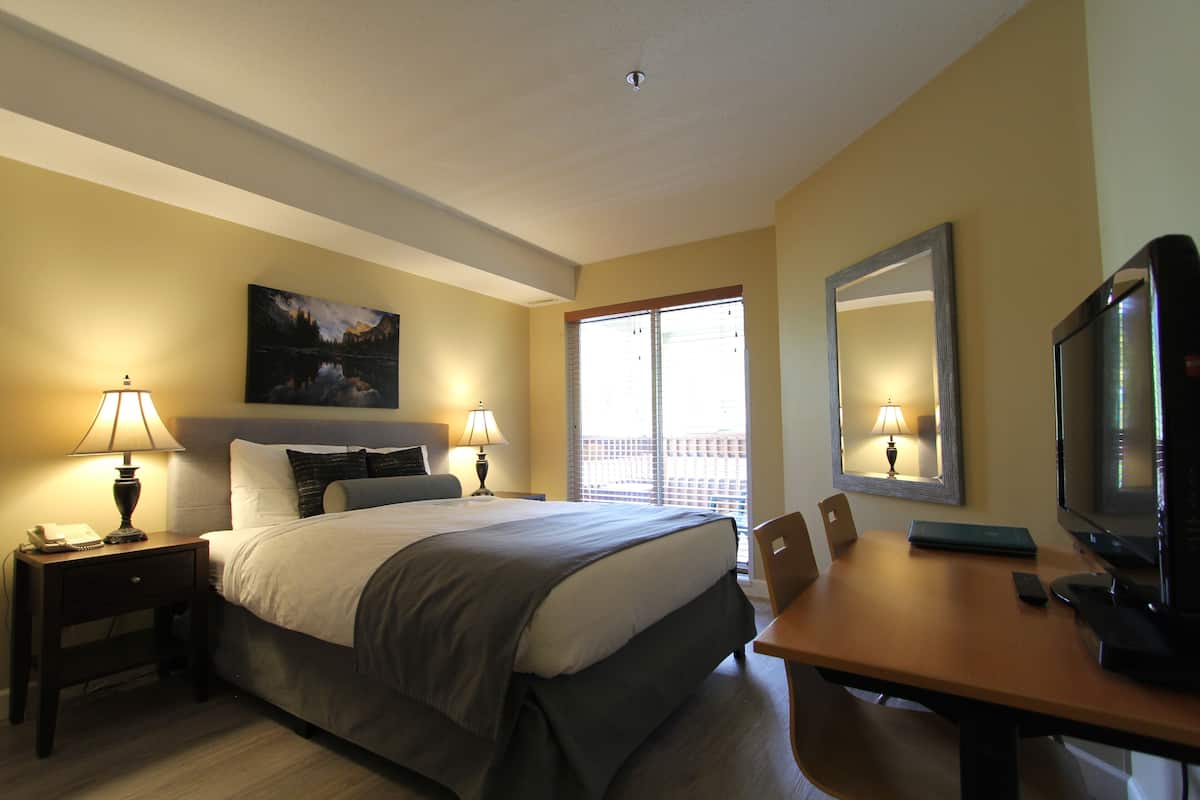 Habitación de hotel con cama, lámparas de noche, escritorio con televisor y ventana con persianas.