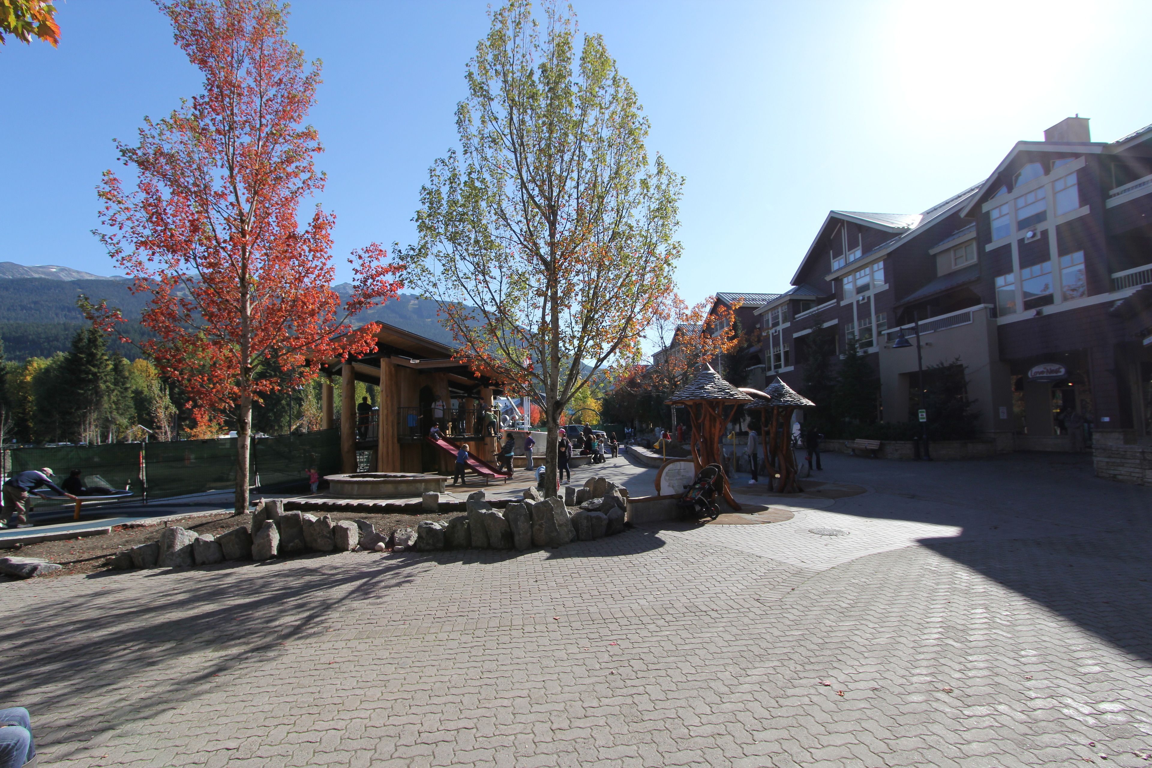 A paved plaza with stone benches, a playground, and a gazebo.