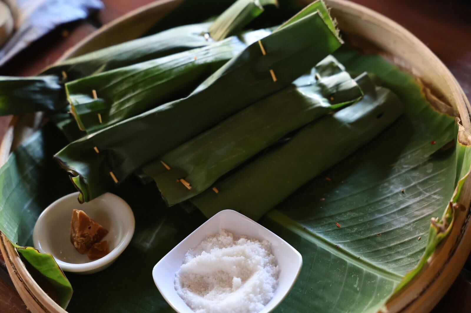 A traditional food presentation with rice wrapped in banana leaves, accompanied by a small bowl of salt and a piece of ginger.