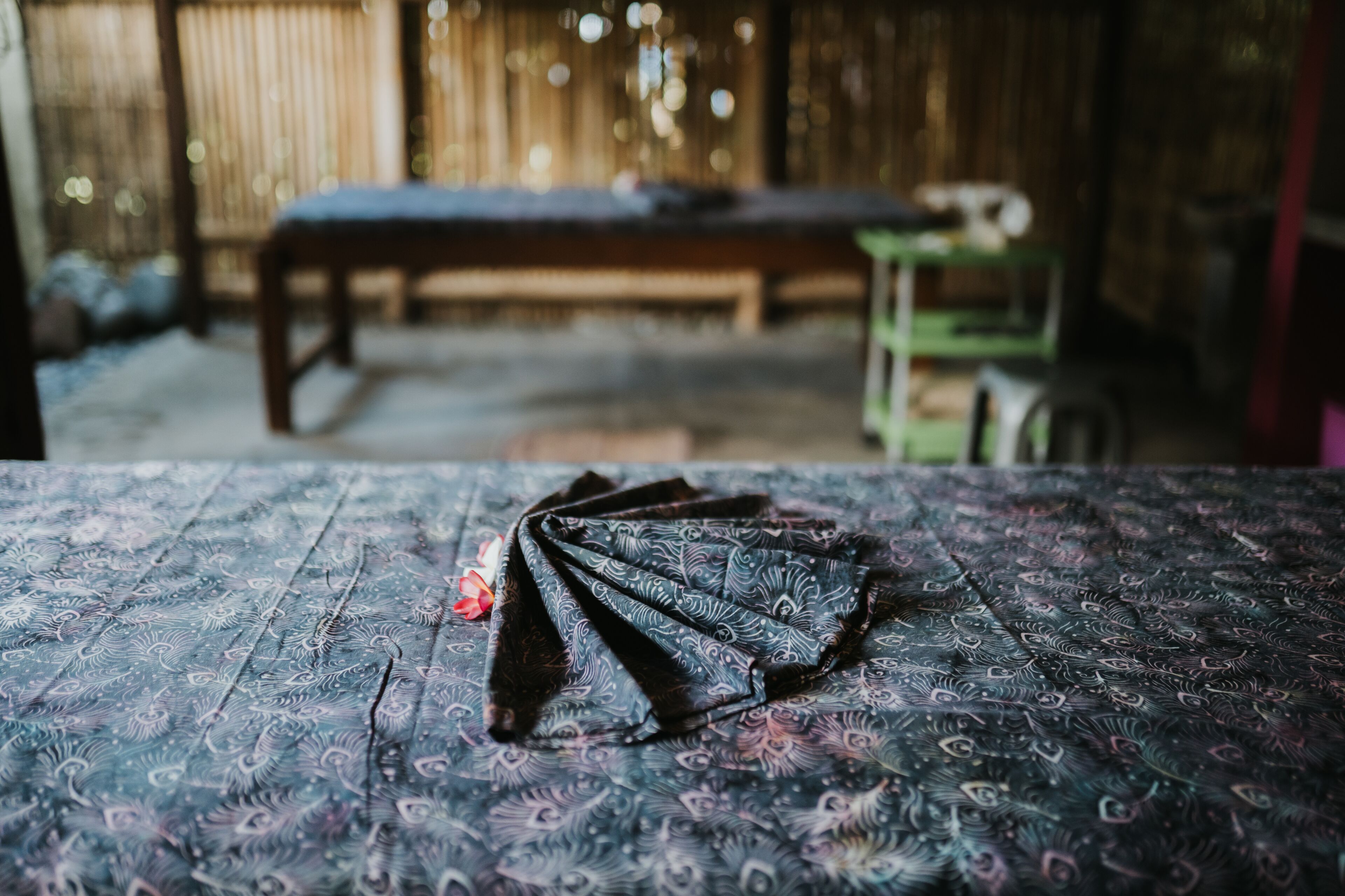 A room with a patterned bedspread, a wooden bench, and a green cart in the background.