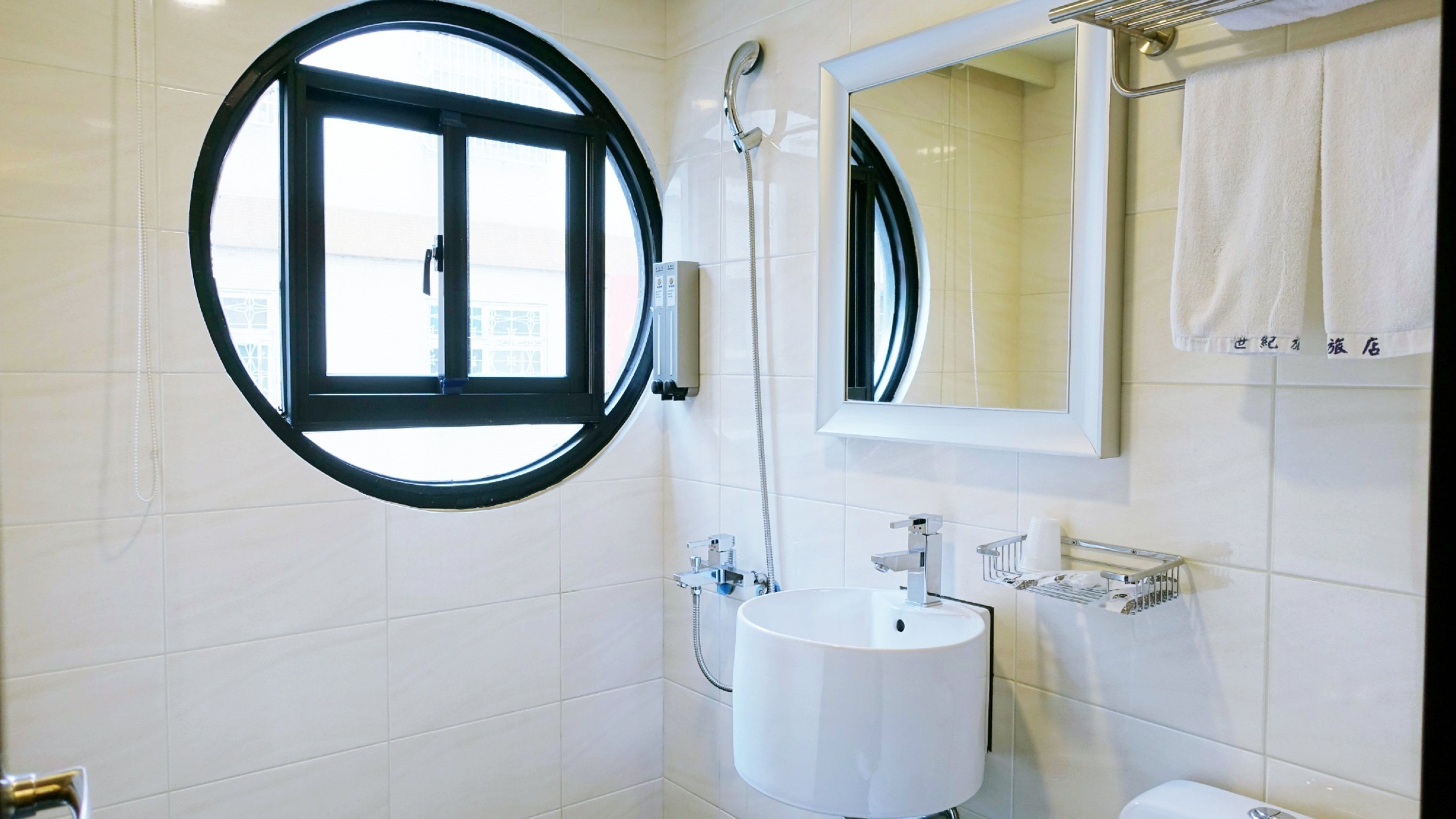 A modern bathroom with a round window, a sink, a mirror, and a towel rack.