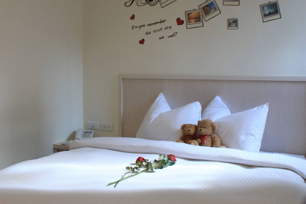 A neatly made bed with white linens, a teddy bear on the pillows, and a wall decal with photos and a camera.