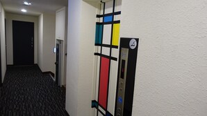 A hallway with a patterned carpet, a door, and an elevator with a colorful stripe design. - Century Hotel (Kaohsiung)