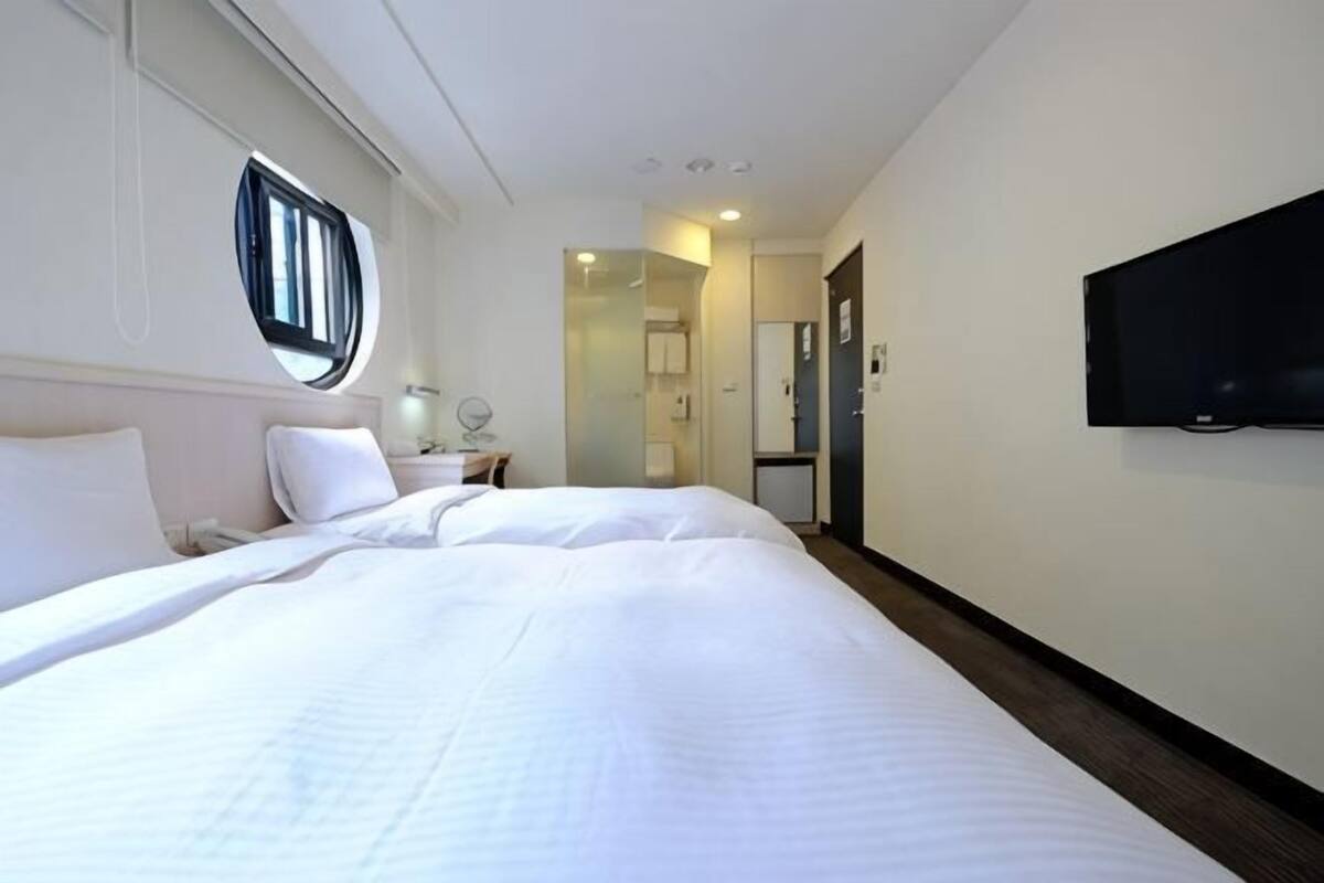 A hotel room with a large bed, a TV mounted on the wall, a window, and a door leading to a bathroom.