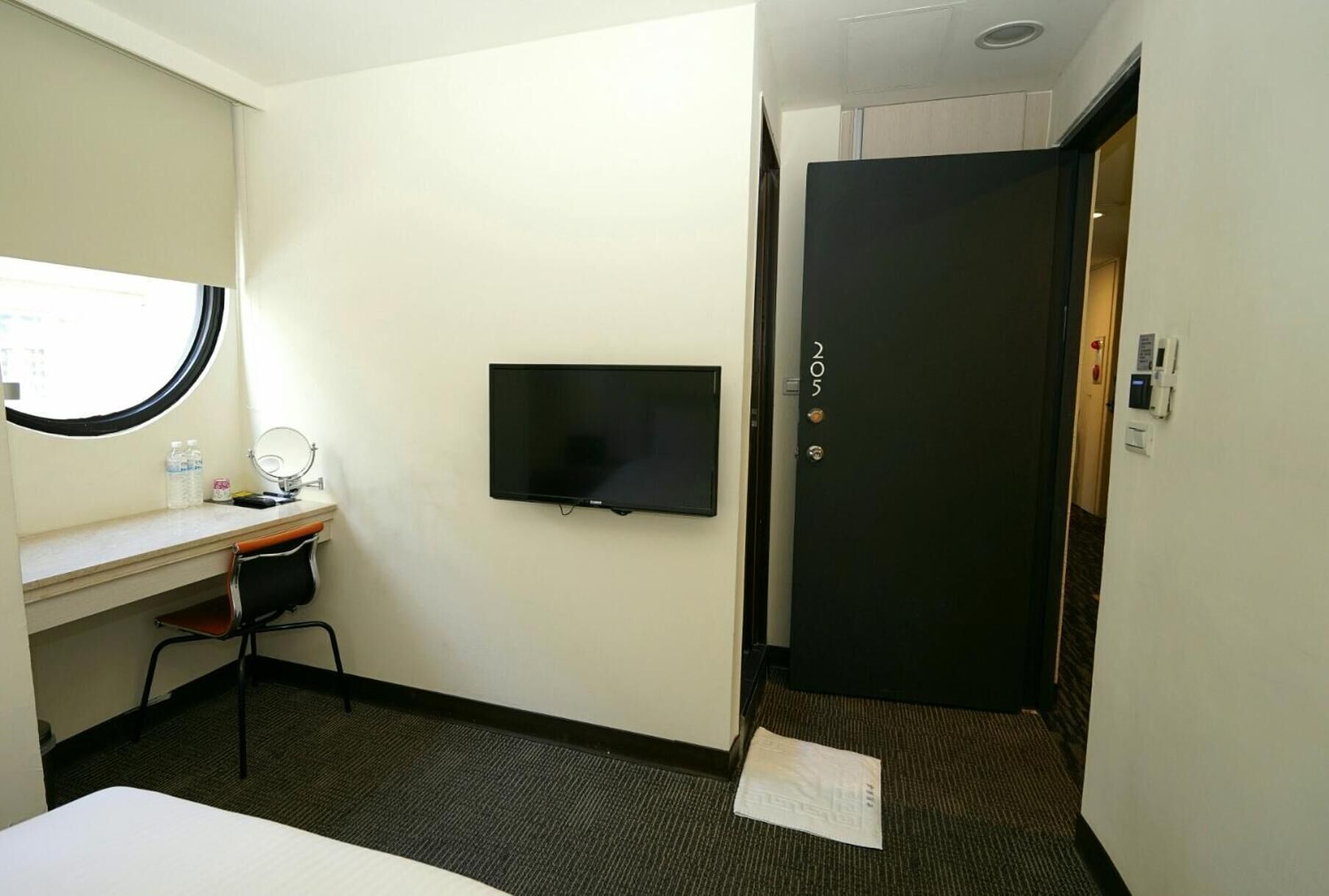 Una camera d'hotel con un letto, una scrivania con un computer, una televisione e una porta con un numero.