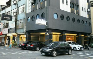 A modern building with a black facade and circular windows. There are cars parked in front, and a few shops on the ground floor. - Century Hotel (Kaohsiung)