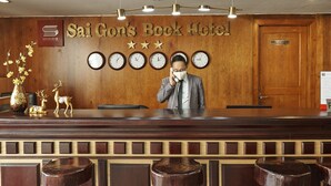 A reception desk at Sai Gon’s Book Hotel with clocks, a phone, and a sign above.