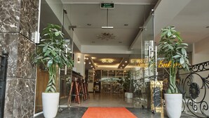 A hotel entrance with marble walls, a red carpeted staircase, and potted plants.