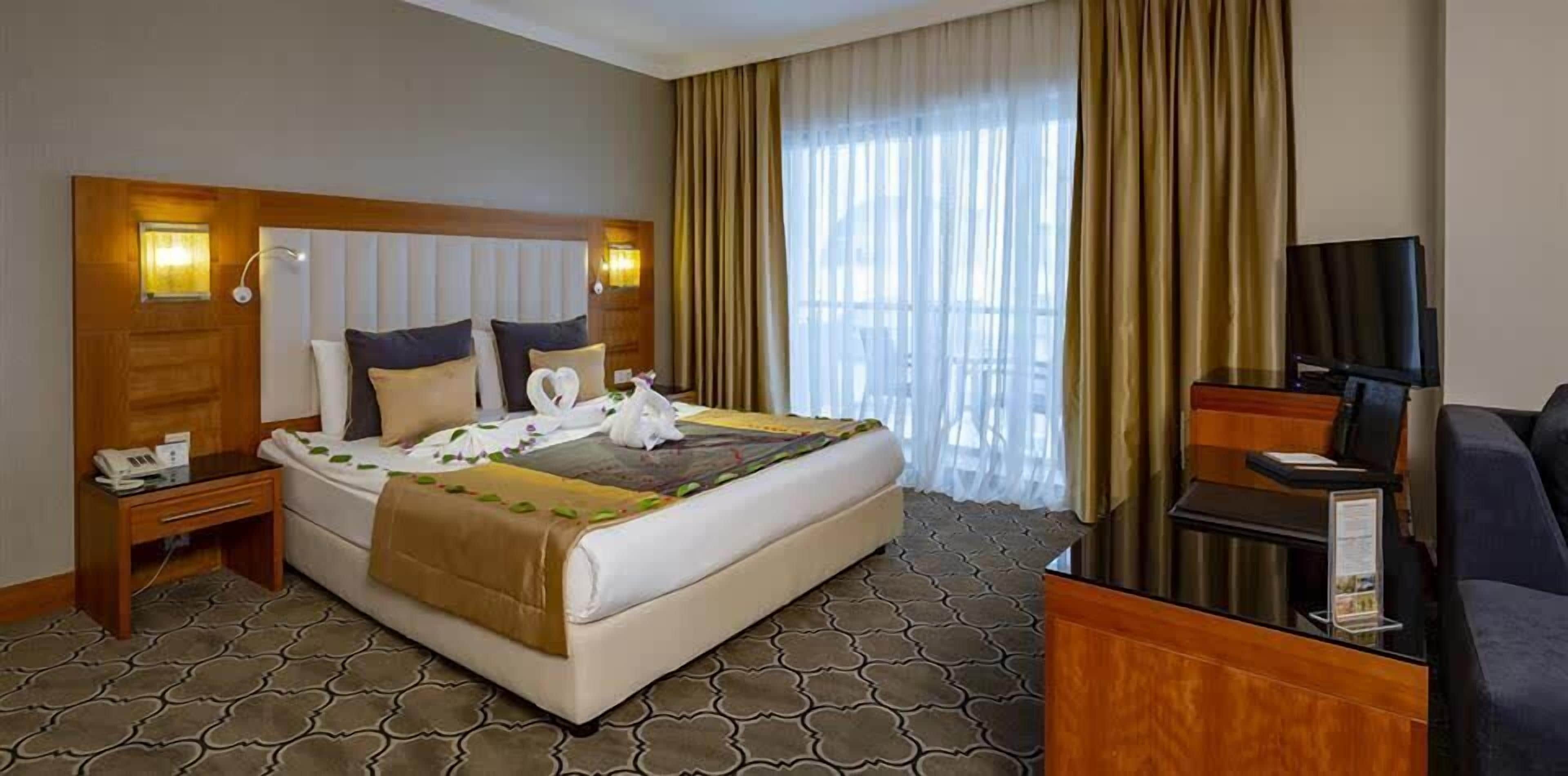 A hotel room with a large bed, a desk, a TV, and a window with curtains.