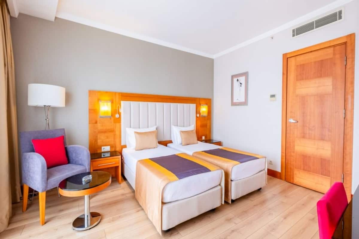 A hotel room with two beds, a chair, a small table, and a wooden door.