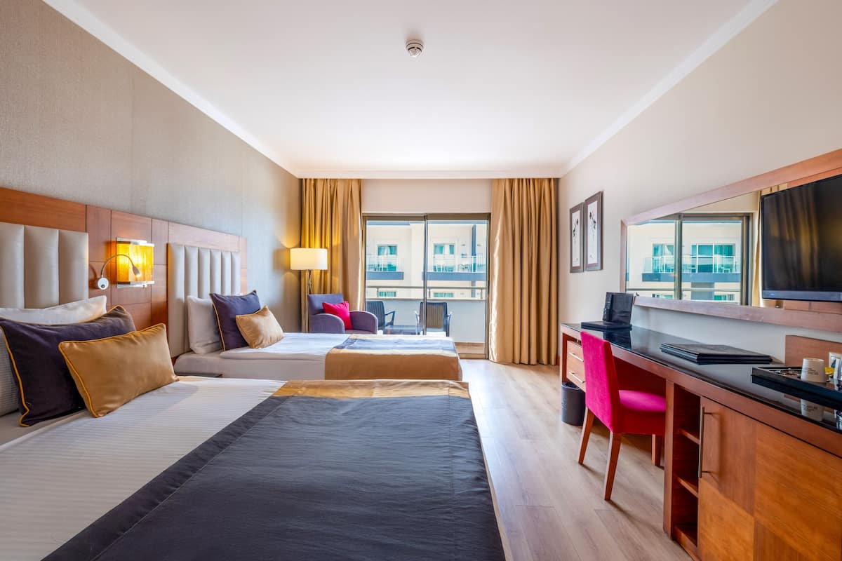 A hotel room with two beds, a desk, a chair, a TV, and a window with curtains.