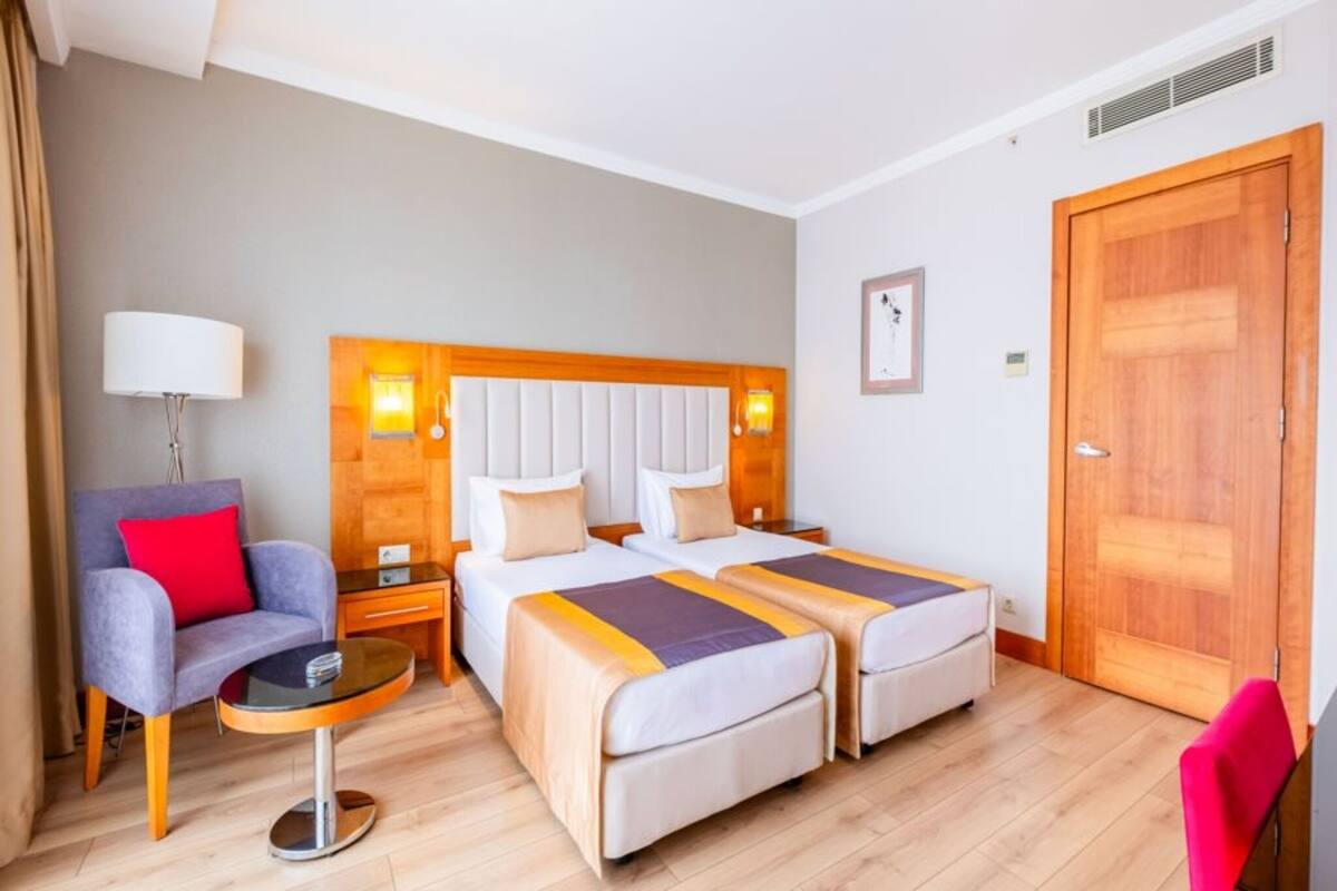 A hotel room with two beds, a chair, a small table, and a wooden door.