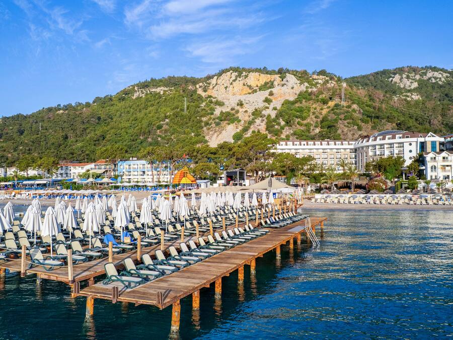 Un hotel frente al mar con un muelle que se adentra en el océano, que cuenta con hileras de tumbonas y sombrillas.