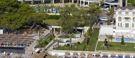 A hotel with a long pier extending into the water, a pool area, and a mountainous backdrop.