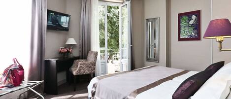 Habitación de hotel con cama, escritorio, silla, televisor y ventana con vista a zonas verdes.