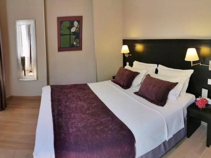 A neatly made bed with a white and purple bedspread, two pillows, and a headboard with wall-mounted lamps.