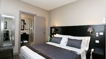 A hotel room with a bed, bedside table, lamp, and a bathroom visible through an open door.