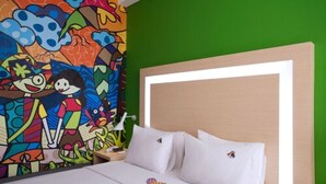 Een hotelkamer met een kleurrijke muurschildering op een wand, een bed met witte lakens, en een groene accentwand.