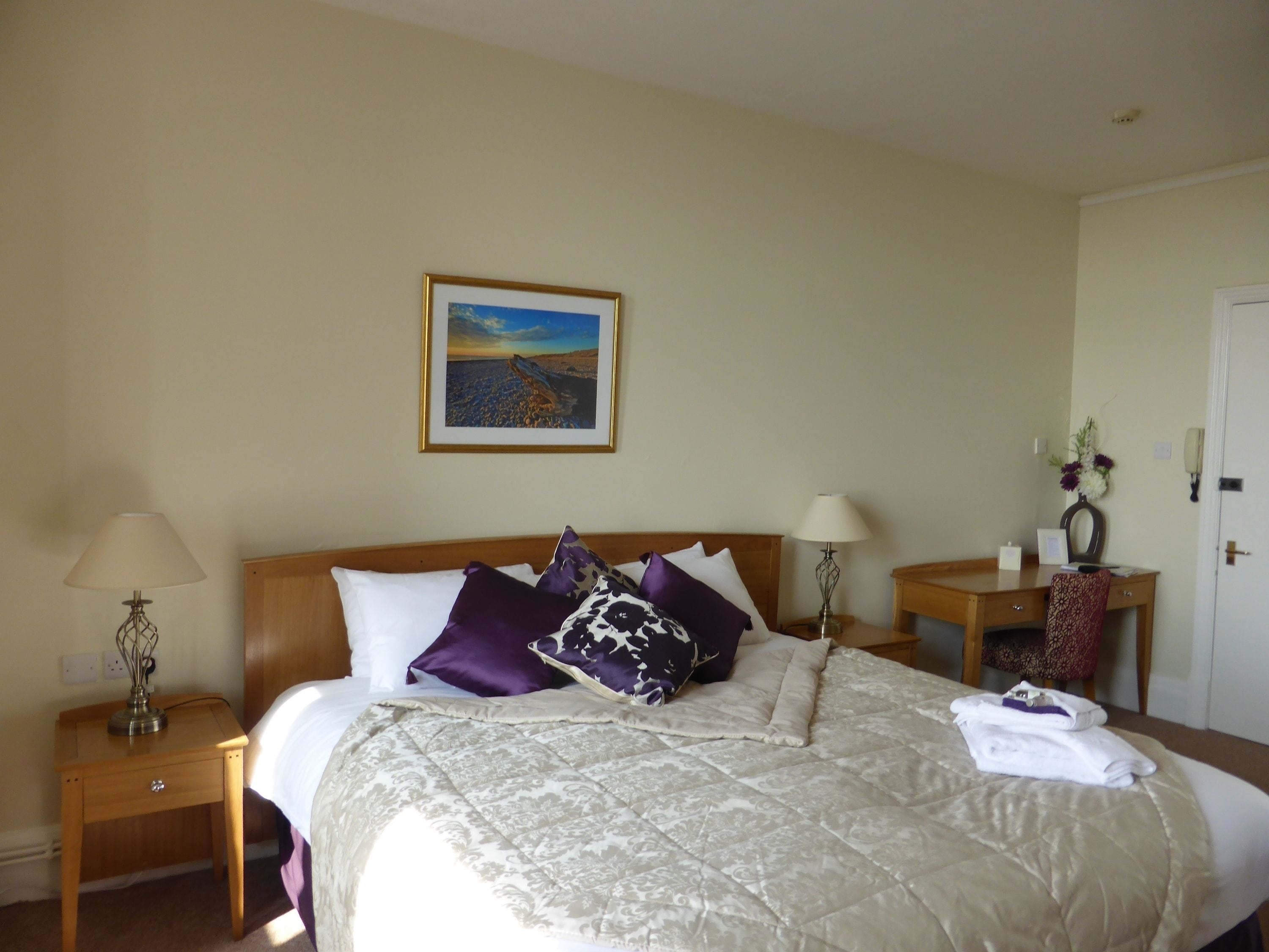 A hotel room with a large bed, two bedside tables, a nightstand, a framed picture on the wall, and a door.