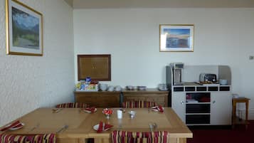 A dining area with a wooden table set for four, striped chairs, a small cabinet with kitchen appliances, and two framed pictures on the walls.