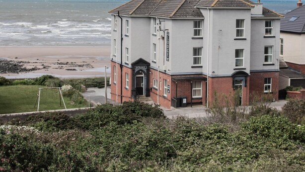A two-story building with a sign reading "Entrance" at the front, located near a beach with visible waves. - Bailey Ground Lodge (Seascale)