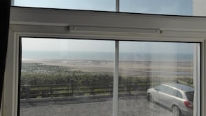A view through a window of a parking area with a car and a landscape with a fence and greenery. - Bailey Ground Lodge (Seascale)