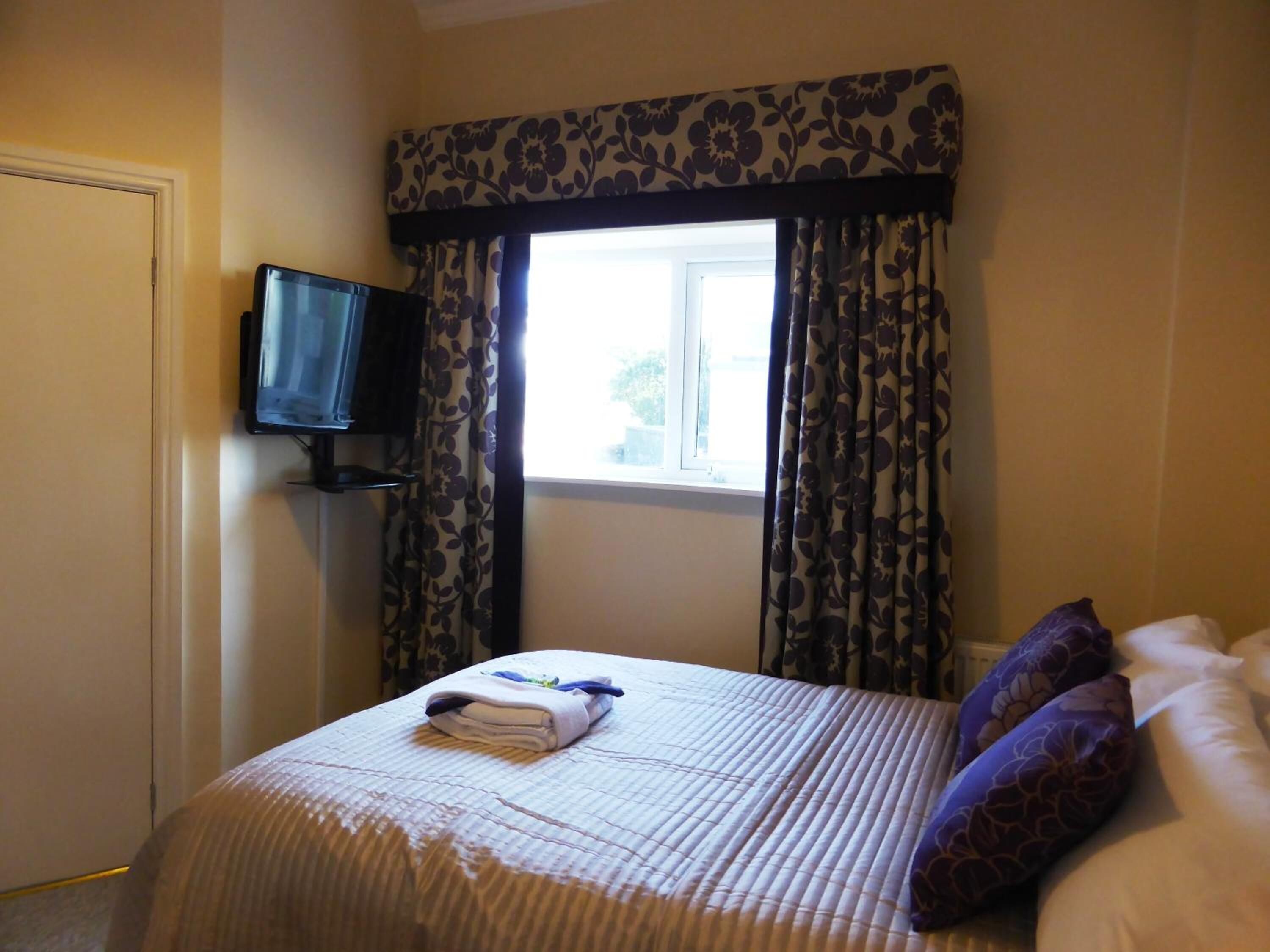 A hotel room with a bed, a television on a stand, and a window with curtains.