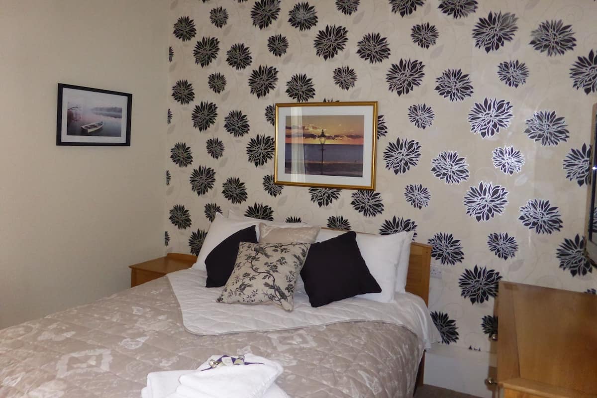 A bedroom with a bed, pillows, a framed picture, and a patterned wallpaper.