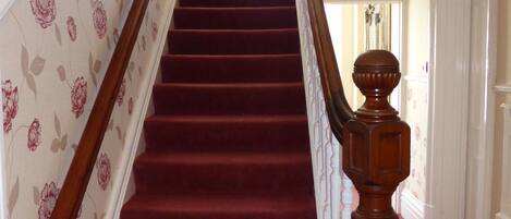 Una escalera con alfombra roja y papel tapiz floral en las paredes.