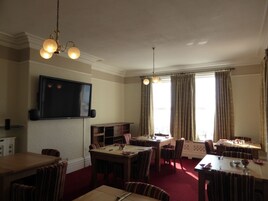 Un comedor con varias mesas y sillas, un televisor montado en la pared y una ventana con cortinas.
