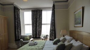 A hotel room with a large bed, a chair, a small table, and a window with curtains. - Bailey Ground Lodge (Seascale)