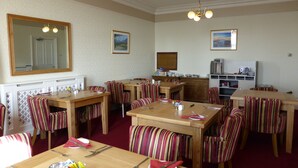 A dining area with striped chairs and tables, a large mirror, and a kitchen area with appliances. - Bailey Ground Lodge (Seascale)
