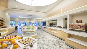 A modern hotel lobby with a central food display, seating area, and a coffee station. - Hotel Asdem Park (Kemer)