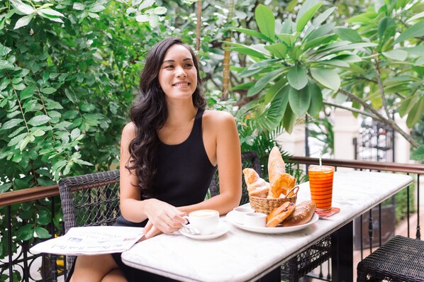A person sitting at an outdoor table with a basket of bread, a cup of coffee, and a glass of orange juice. - Central Mansions Hotel and Apartments (Phnom Penh)