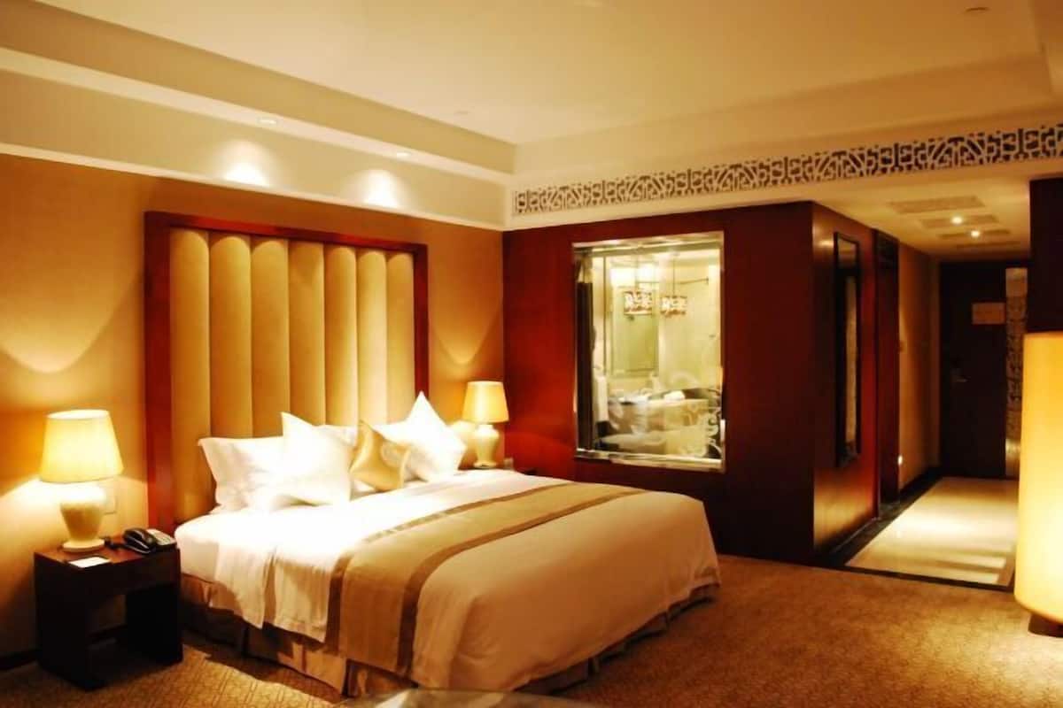 A hotel room with a large bed, two bedside lamps, a nightstand, and a mirror.