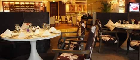 A restaurant with round tables, chairs with floral upholstery, and a bar area in the background.