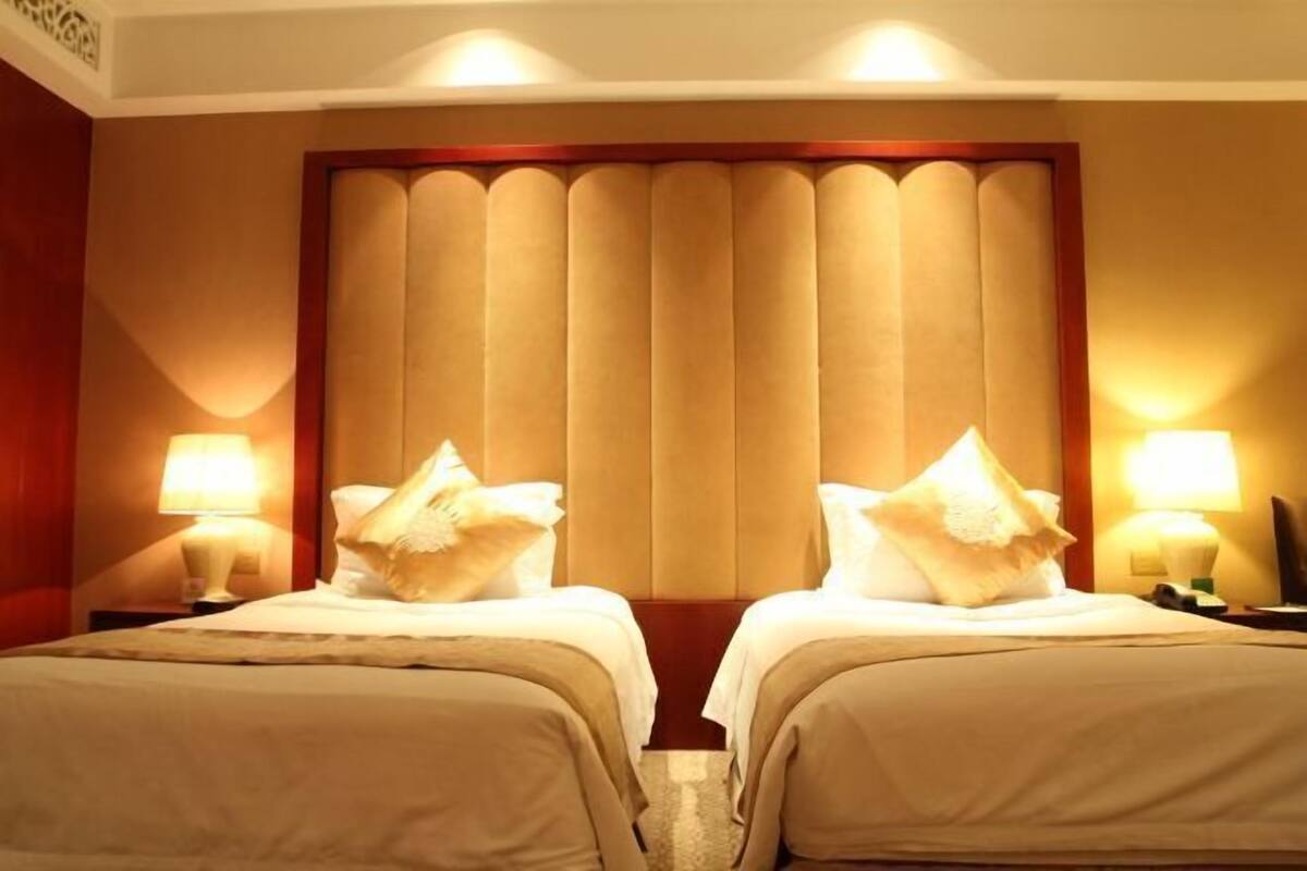 A hotel room with two beds, each with a pillow and a nightstand with a lamp.