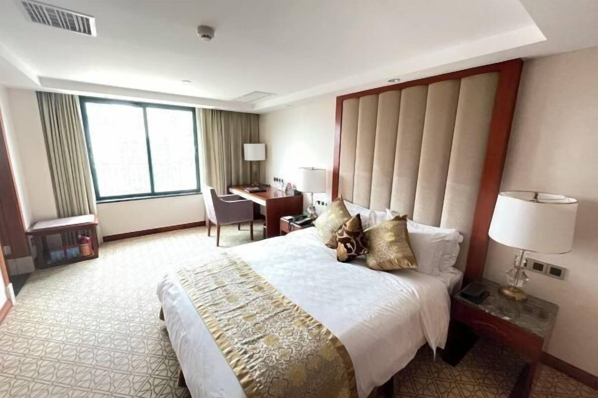 A hotel room with a large bed, a desk, a chair, a nightstand, and a window with curtains.