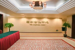 Une salle de conférence avec un tapis à motifs, une table verte et un lustre.