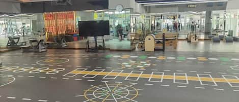 Een ruime binnenruimte met fitnessapparatuur, een groot scherm en een vloer met patroon.