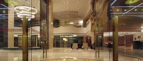 A spacious lobby with a high ceiling, glass walls, and a central chandelier.