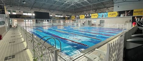 An indoor swimming pool with lanes, a high ceiling, and a tiled floor.