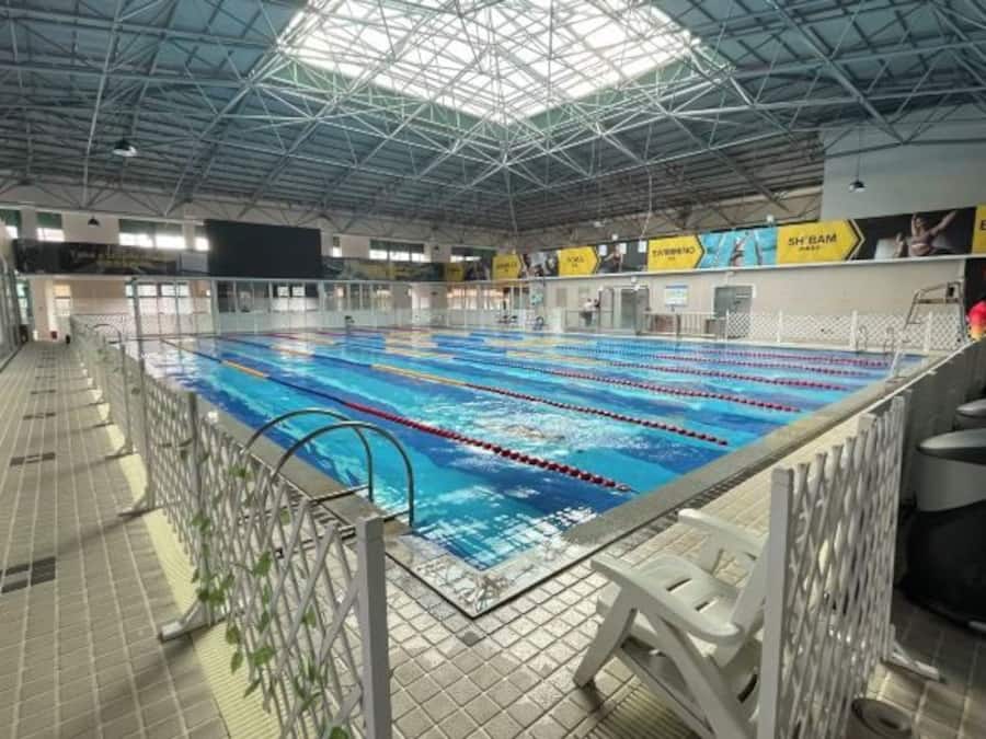 An indoor swimming pool with lanes, a high ceiling, and a tiled floor.