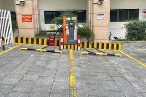 Un área de estacionamiento con bomba de combustible, barreras de seguridad amarillas y negras, y una entrada con portón.