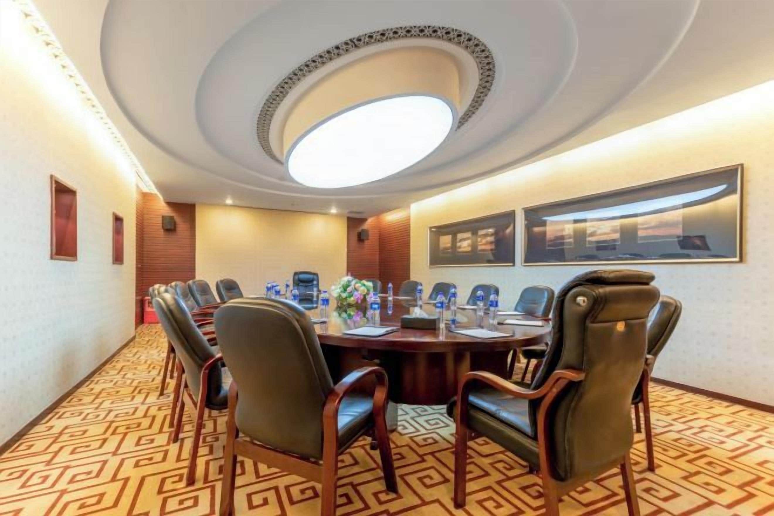 A conference room with a long table, chairs, a ceiling light, and framed pictures on the wall.