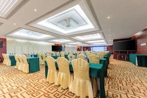 Une salle de conférence avec des rangées de tables et de chaises, un grand écran et une moquette à motifs.